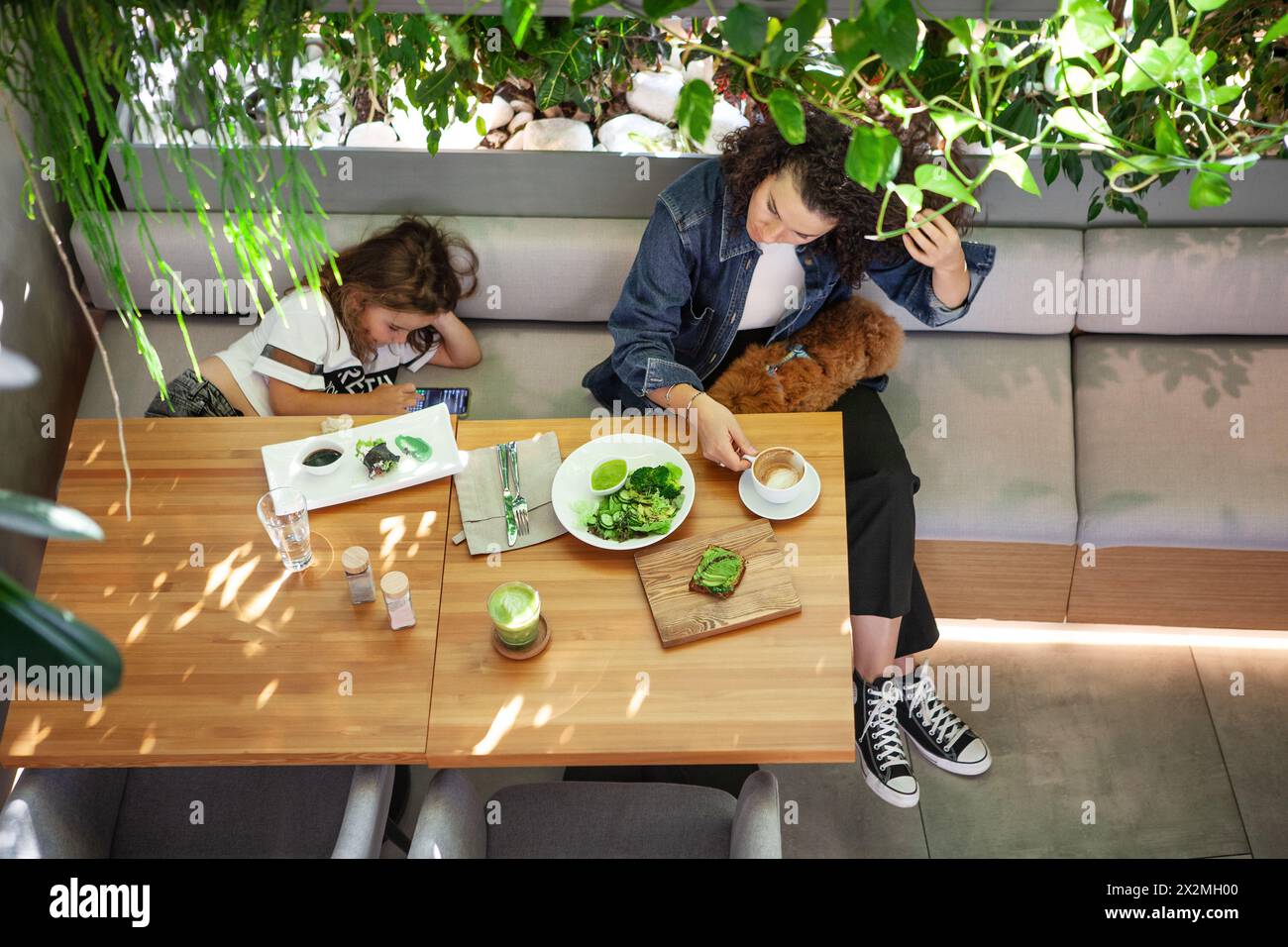 Familie Mutter Tochter und Hund, essen Sie im lebhaften veganen Restaurant, genießen Sie das Essen umgeben von üppigem Grün und genießen Sie pflanzlichen Lebensstil mit gesunder Ernährung Stockfoto