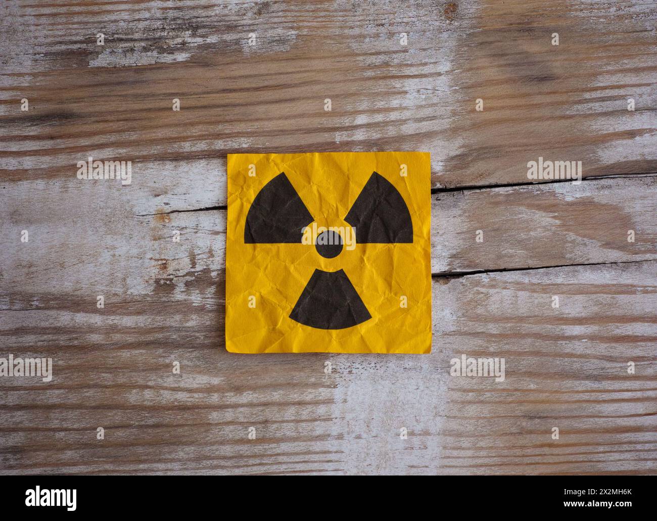 Gelbes Papier mit Strahlenwarnschild auf Holzoberfläche. Stockfoto