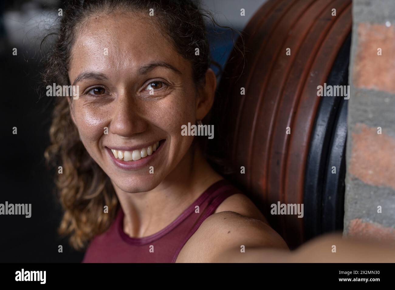 Lächelnde lateinamerikanische Frau ist im Fitnessstudio und benutzt ihr Handy, um ein Selbstporträt zu machen. Gesunder Lebensstil und Kommunikationskonzept Stockfoto