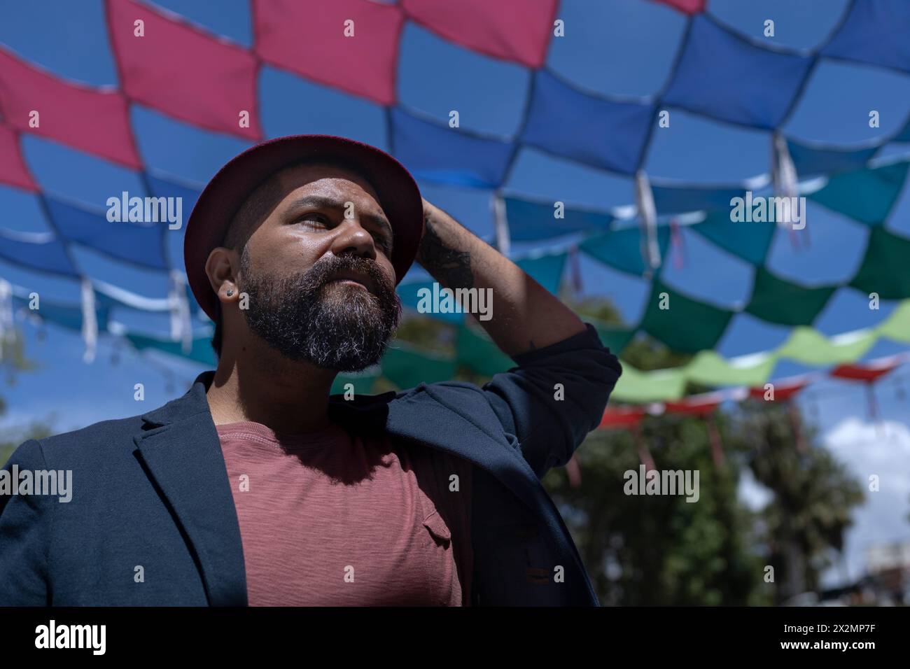 Porträt eines lateinamerikanischen Künstlers mit Bart, Hut und Jacke. Hintergrund farbenfroher Flaggen. Reale Menschen verstehen. Stockfoto