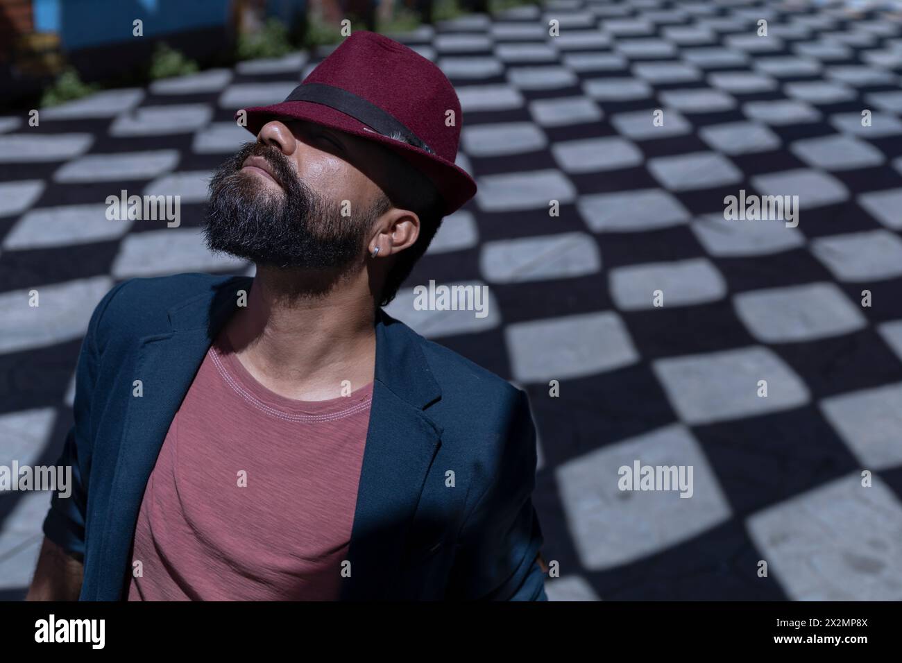 Porträt eines lateinamerikanischen Künstlers mit Bart, Hut und Jacke. Er trägt seinen Hut auf komische Art und Weise und versteckt sein Gesicht. Hintergrund von Schatten mit r Stockfoto