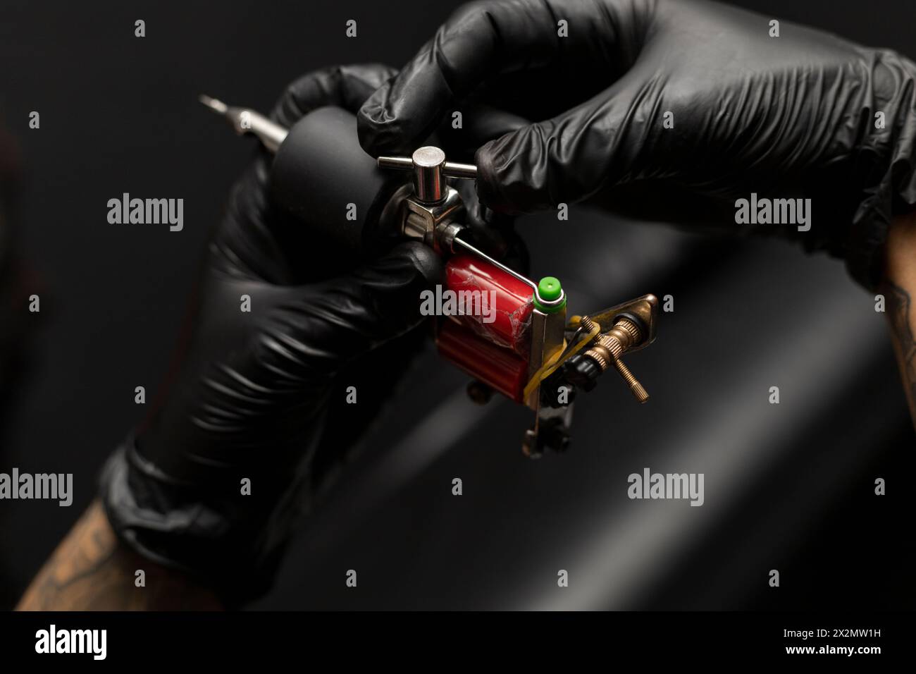 Der Tätowierer stellt seine Tätowiermaschine ein und stellt sie ein. Tragen Sie schwarze Handschuhe. Body-Art-Konzept Stockfoto