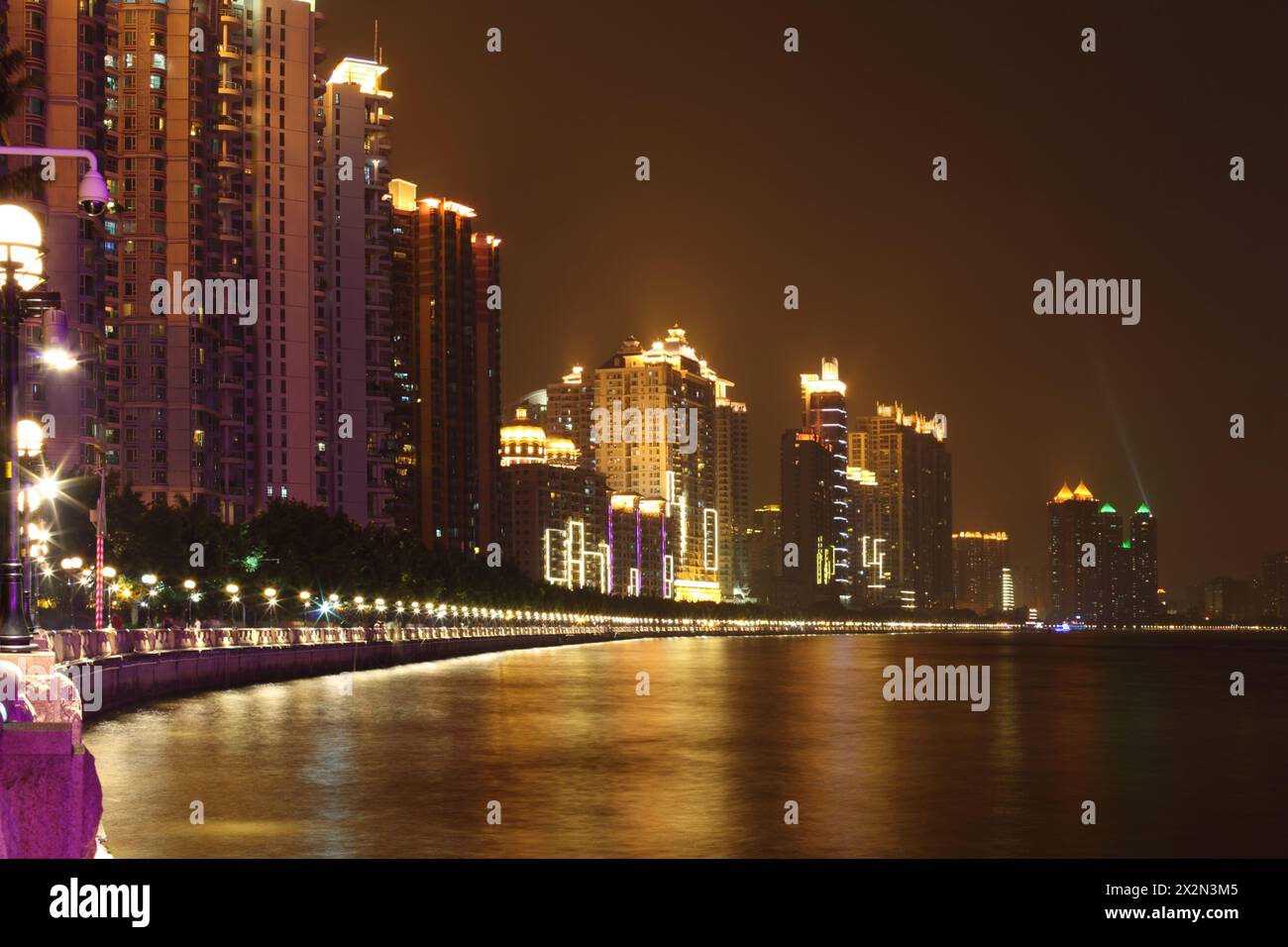 Hohe Gebäude mit Neonbeleuchtung an der Küste in der Nähe des Pearl River mit Farbreflexionen bei Nacht in Guangzhou, China Stockfoto