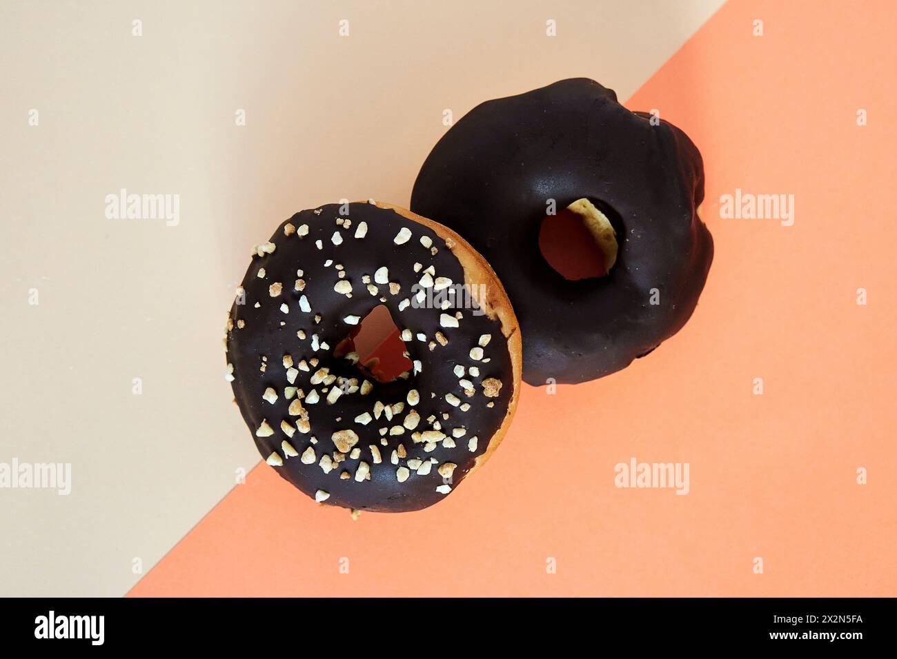 Zwei Donuts mit Schokoladenüberzug und Zerkleinerungsnüssen darauf. Zenithalwinkel auf farbigem Hintergrund Stockfoto