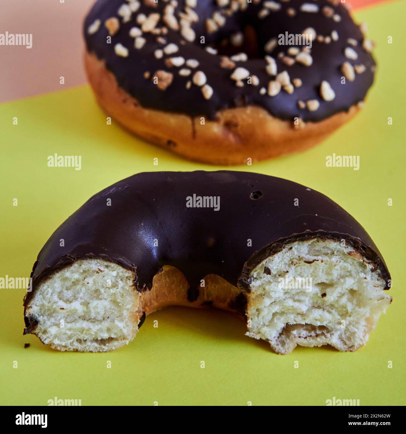 Ein halber, mit Schokolade überzogener Donut auf grünem Hintergrund, ein ganzer Donut im Hintergrund ist unscharf. Quadratisches Format. Stockfoto