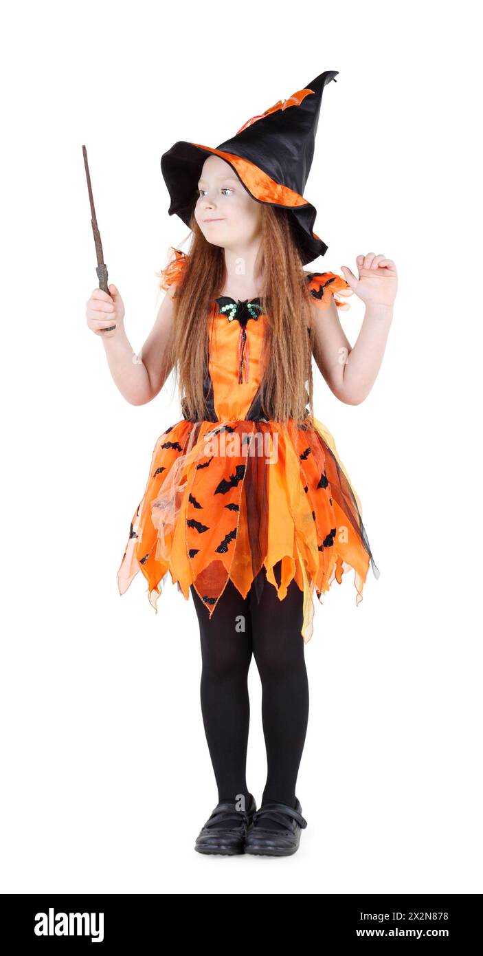 Kleines Mädchen in orangefarbenem Hexenkostüm für Halloween hält und schaut auf den Zauberstab isoliert auf weißem Hintergrund. Stockfoto