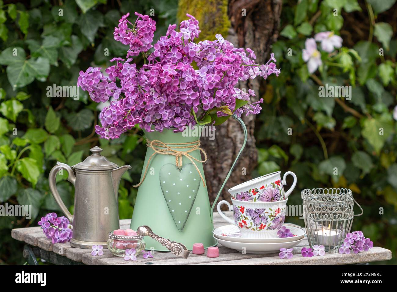 Tisch mit Fliederstrauß, Vintage-Tassen, Kaffeekanne und Tischlaterne Stockfoto