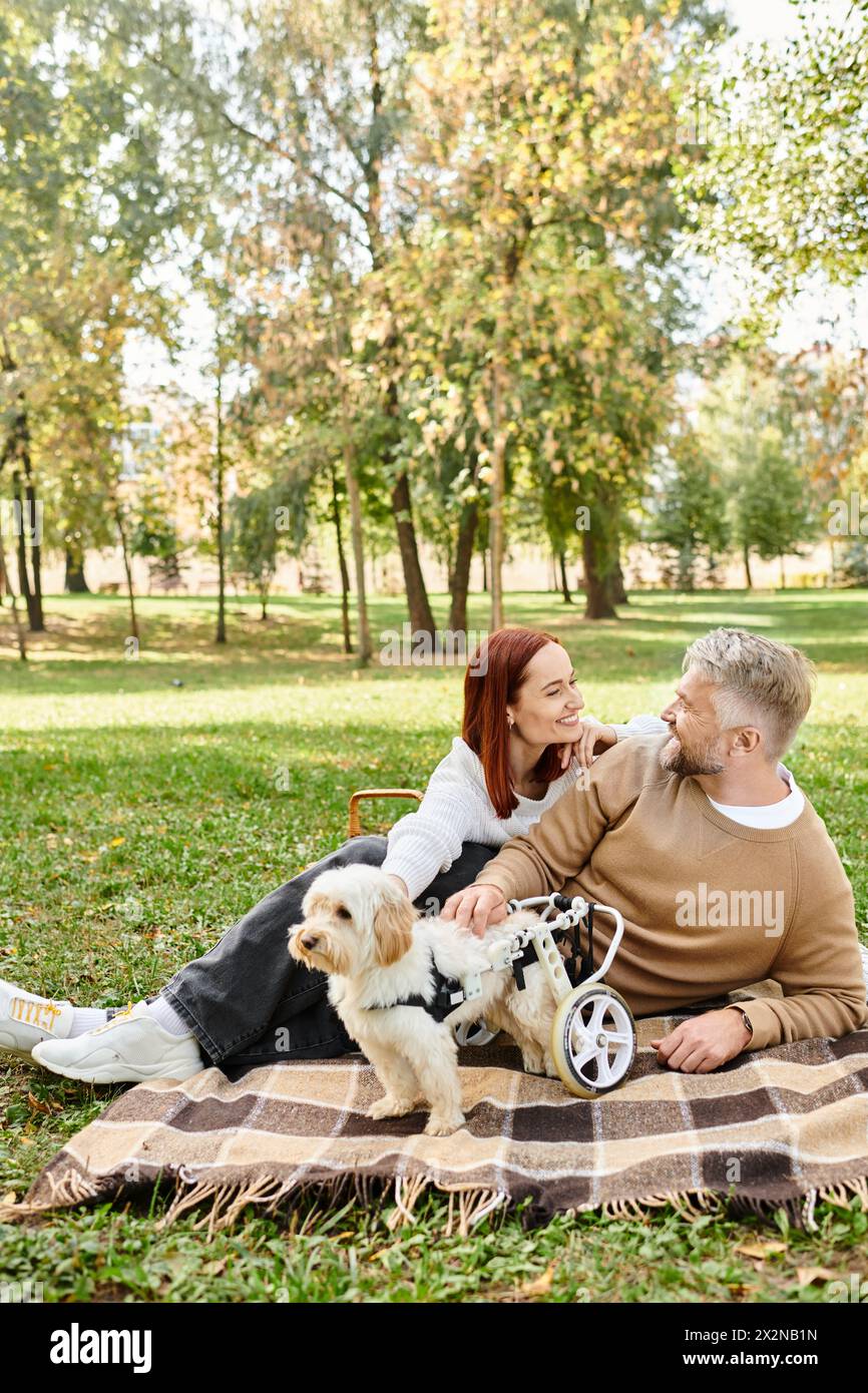 Ein Mann und eine Frau sitzen mit ihrem Hund in einem Park auf einer Decke. Stockfoto