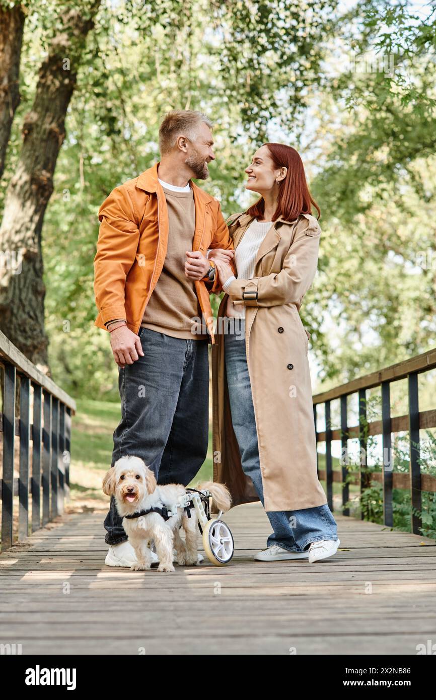 Ein Mann und eine Frau in lässiger Kleidung stehen auf einer Brücke mit ihrem Hund im Park. Stockfoto