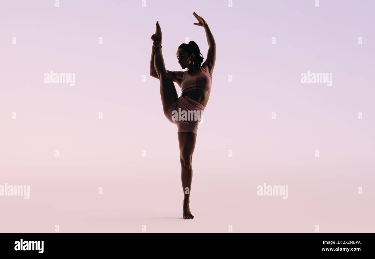 Eine Turnerin zeigt ihre Beweglichkeit und Flexibilität in einem Studio und führt eine künstlerische Routine durch. Mit perfektem Gleichgewicht auf einem Bein zeigt sie t Stockfoto
