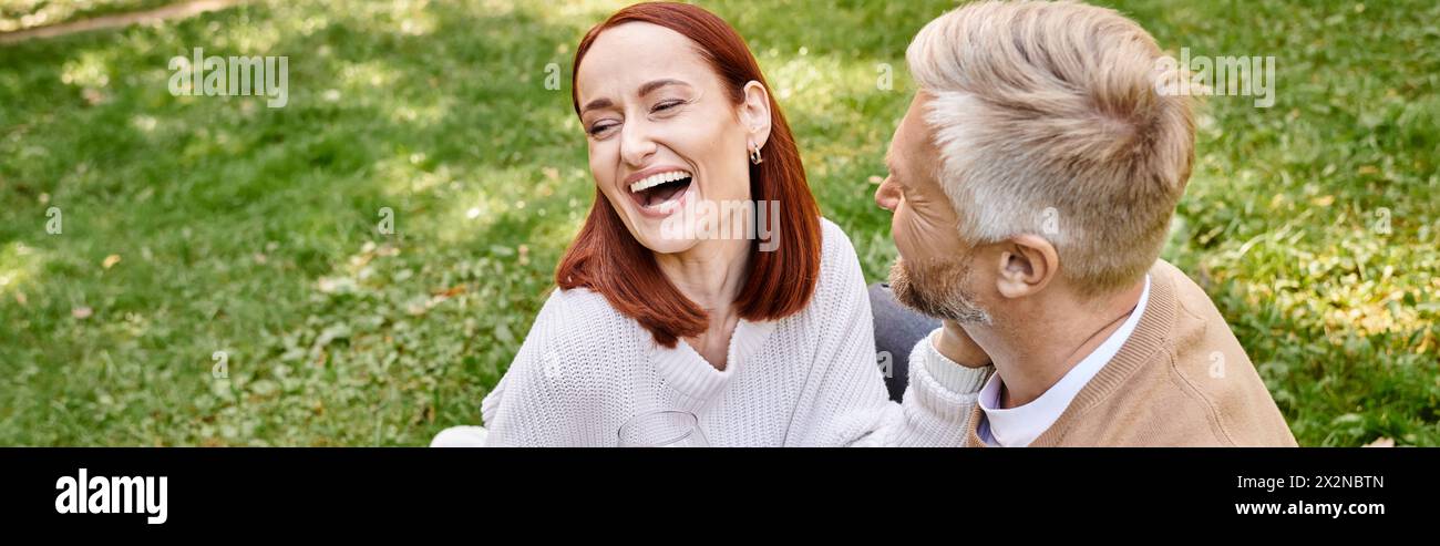 Ein Mann und eine Frau lachen fröhlich, während sie sich gegenseitig in einem grasbewachsenen Feld amüsieren. Stockfoto