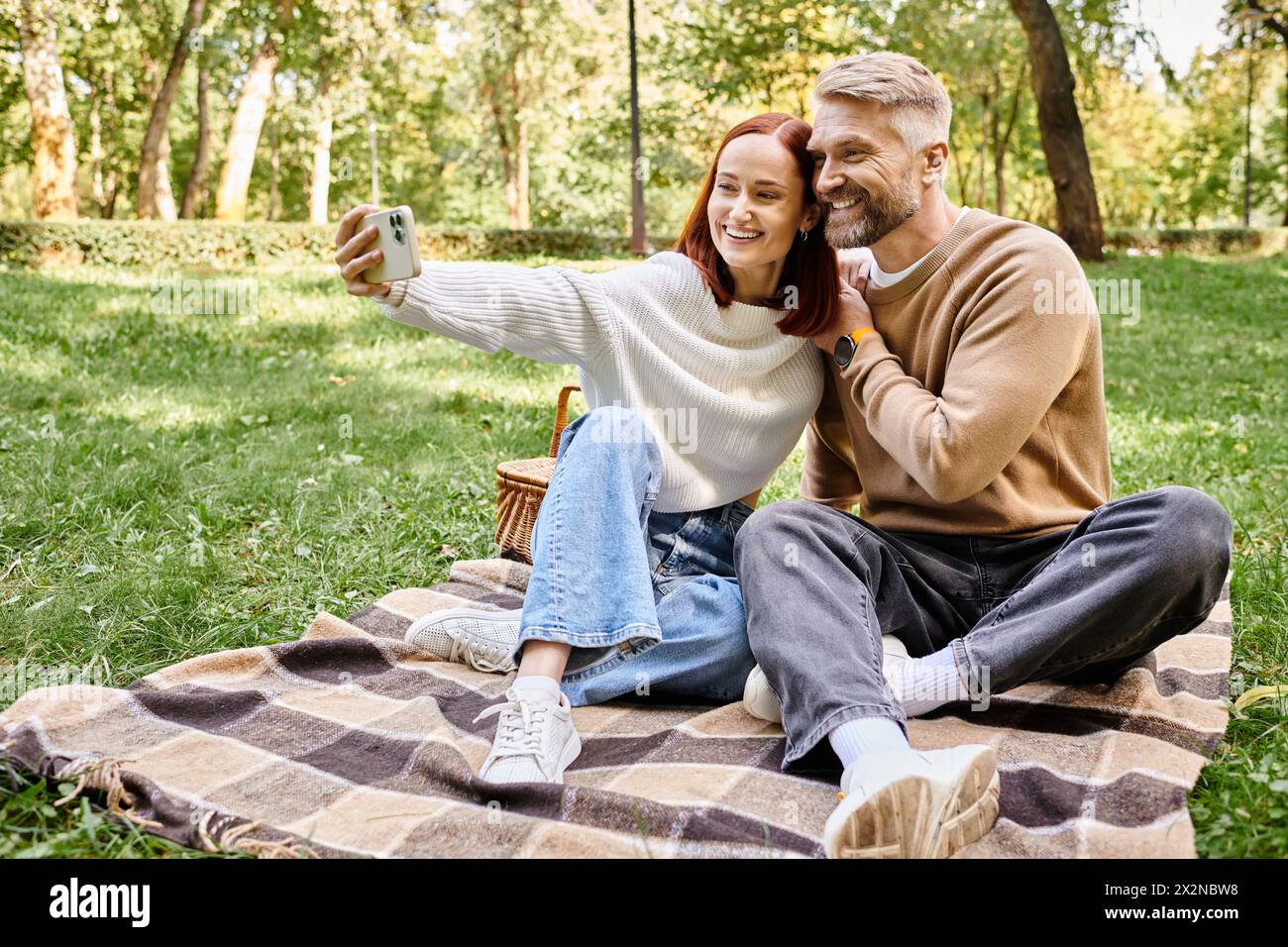 Mann und Frau im Park, sitzen auf einer Decke, fangen den Moment mit Selfie ein. Stockfoto