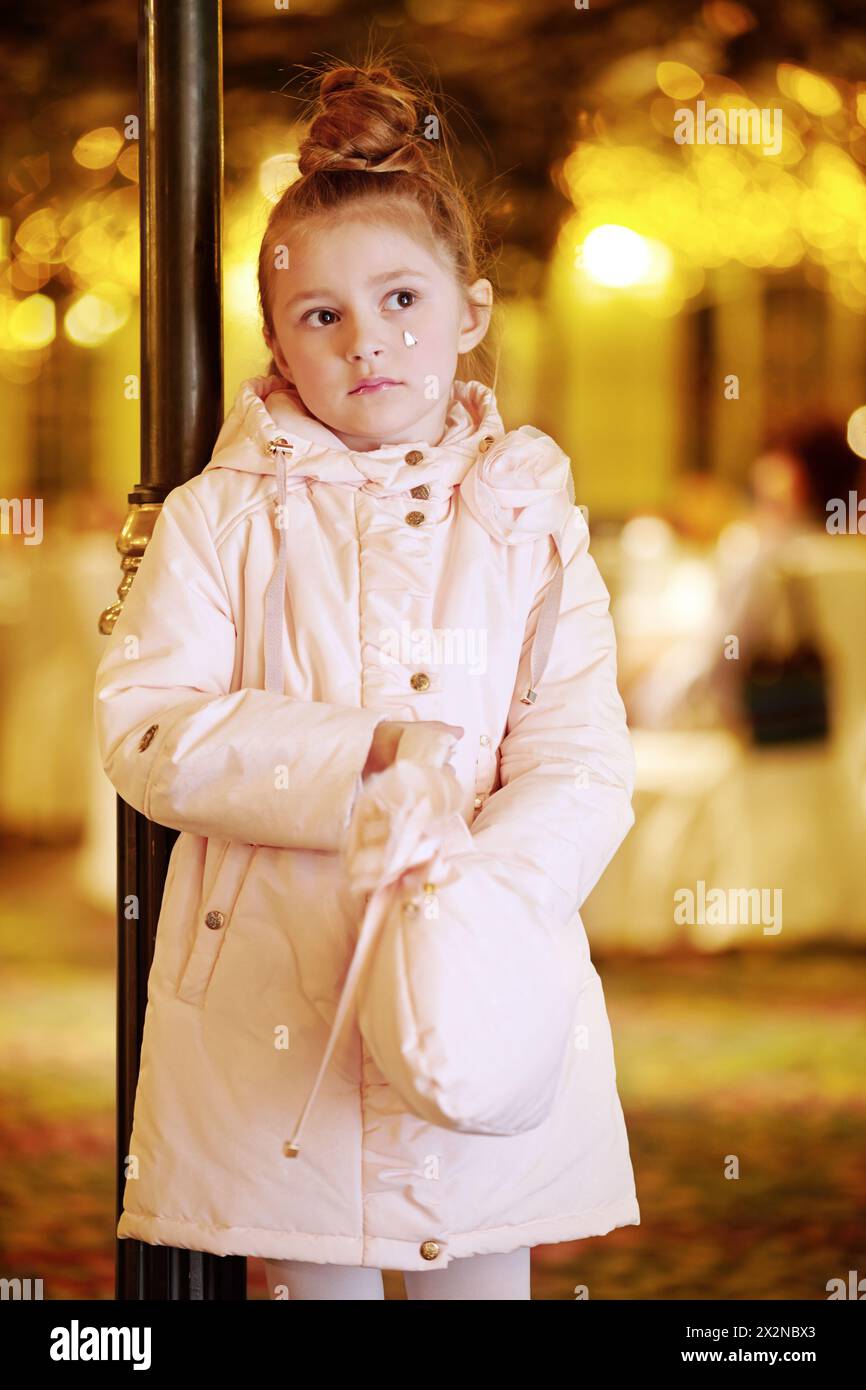 Ein kleines Mädchen im hellen Mantel steht nachdenklich in ihrer Handtasche Stockfoto