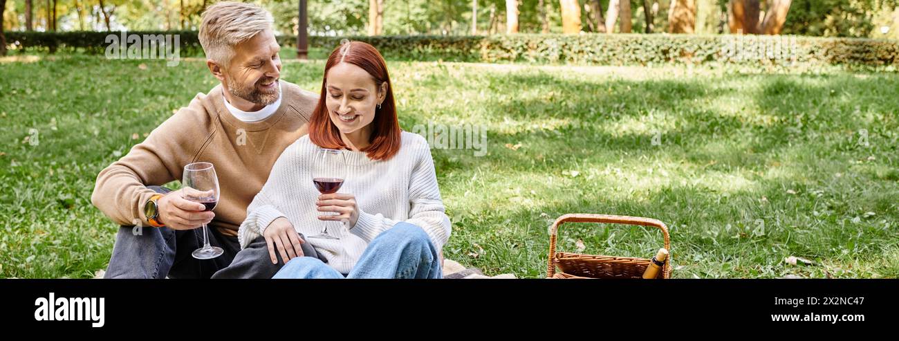Erwachsene Männer und Frauen sitzen auf einer Decke und halten Weingläser in einem Park. Stockfoto Erwachsene Männer und Frauen sitzen auf einer Decke und halten Weingläser in einem Park. Stockfoto