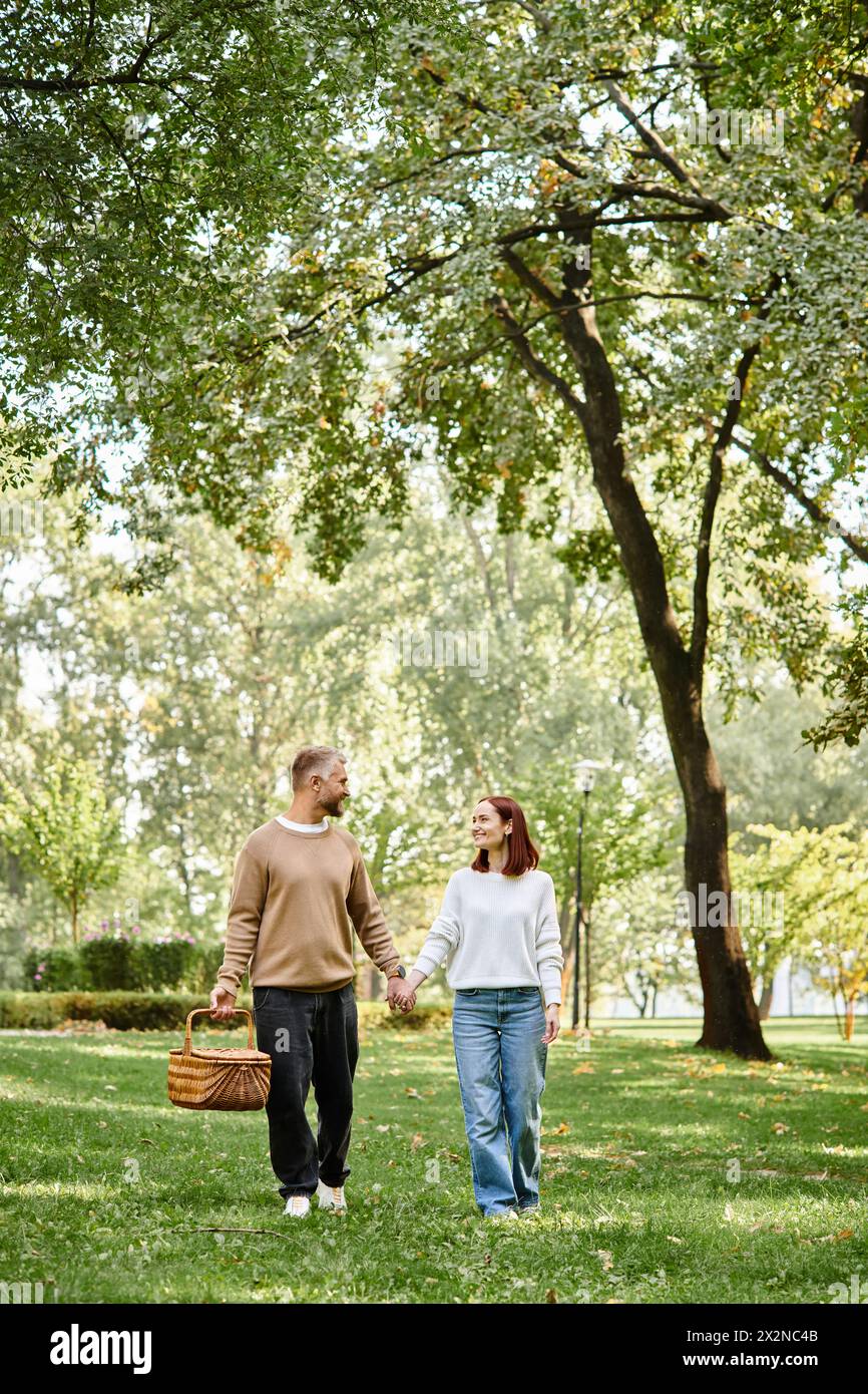 Mann und Frau in lässiger Kleidung halten Hände, gehen durch den Park. Stockfoto