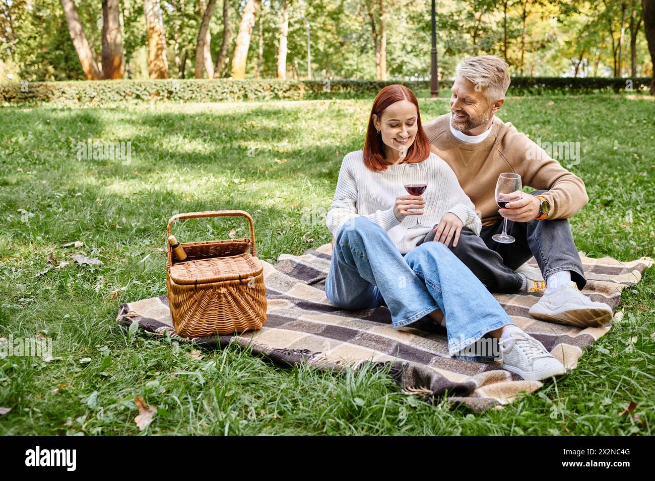 Ein Mann und eine Frau sitzen auf einer Decke im Gras und genießen einen friedlichen Tag im Park. Stockfoto