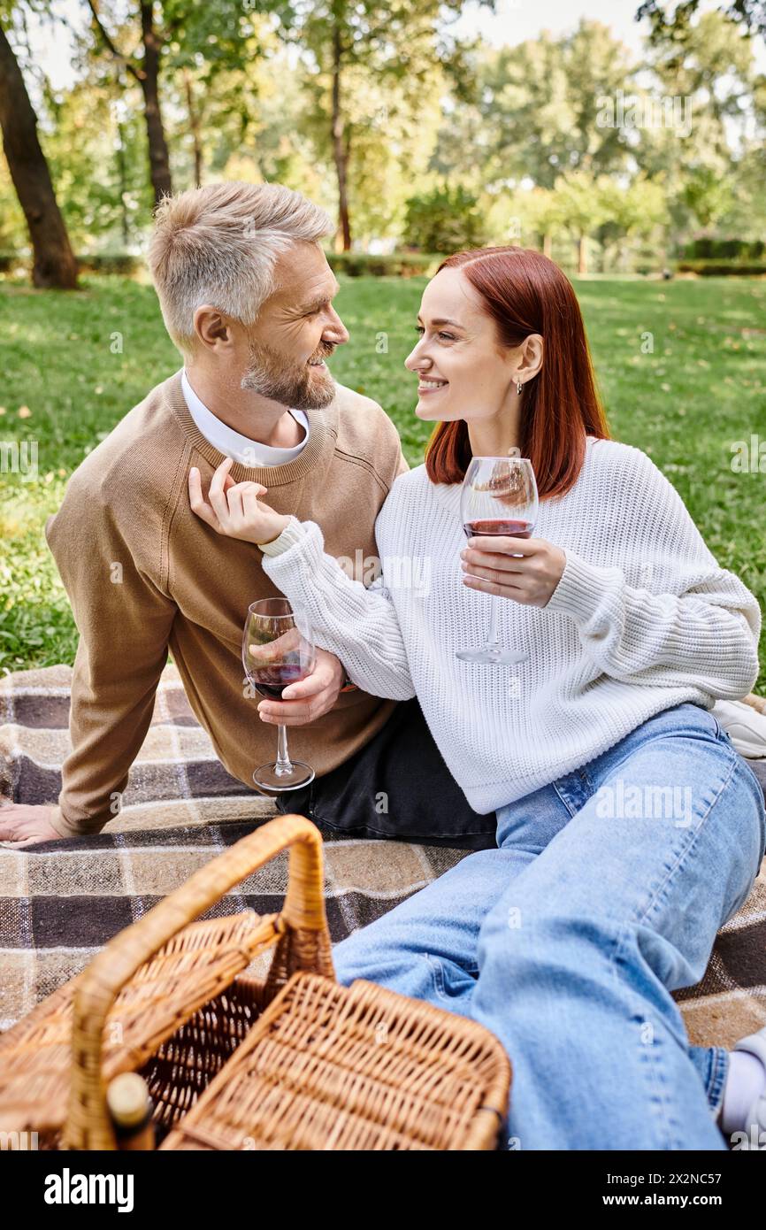 Ein Mann und eine Frau sitzen auf einer Decke im Park und halten Weingläser. Stockfoto
