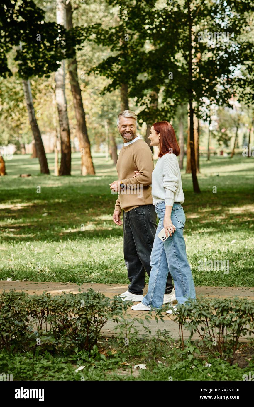Ein Mann und eine Frau, ein liebevolles Paar, schlendern in lässiger Kleidung durch einen Park. Stockfoto