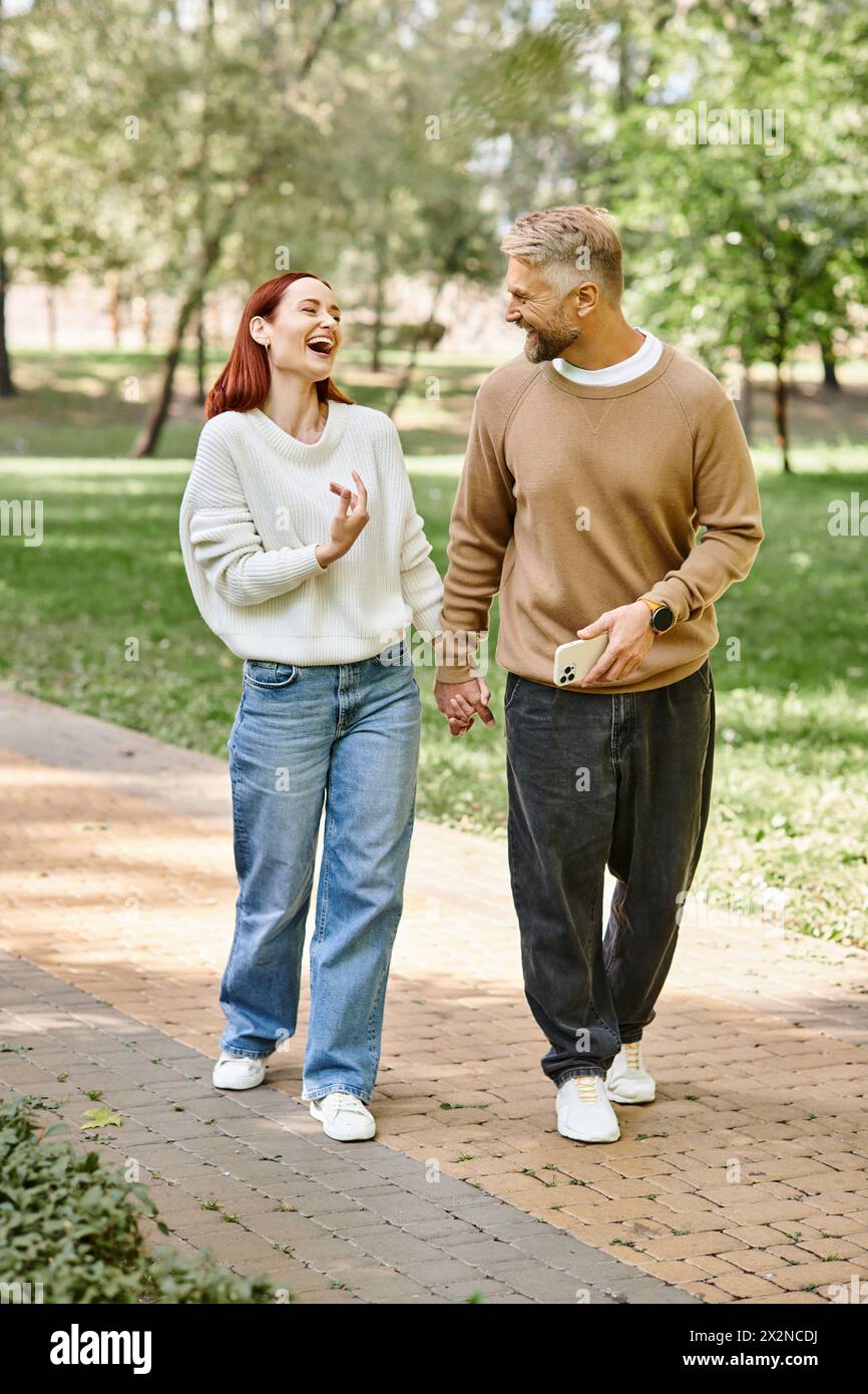 Ein Mann und eine Frau in lässiger Kleidung gehen zusammen auf einem Bürgersteig in einem Park. Stockfoto