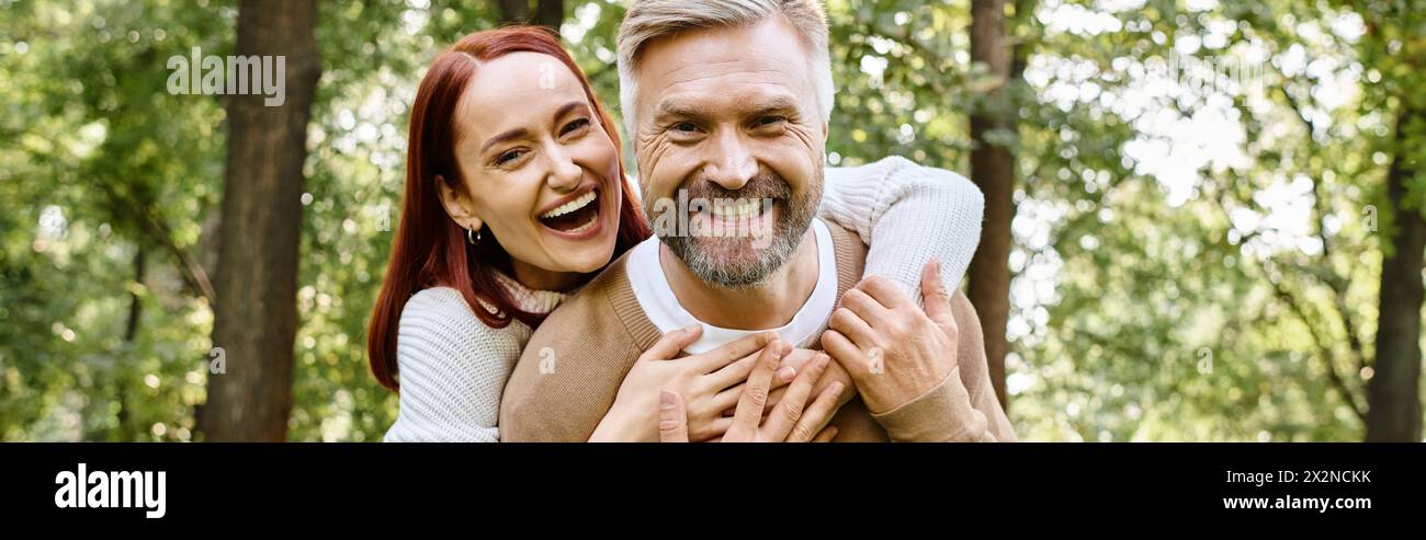 Ein Mann trägt liebevoll eine Frau auf dem Rücken zwischen den Bäumen im Wald. Stockfoto