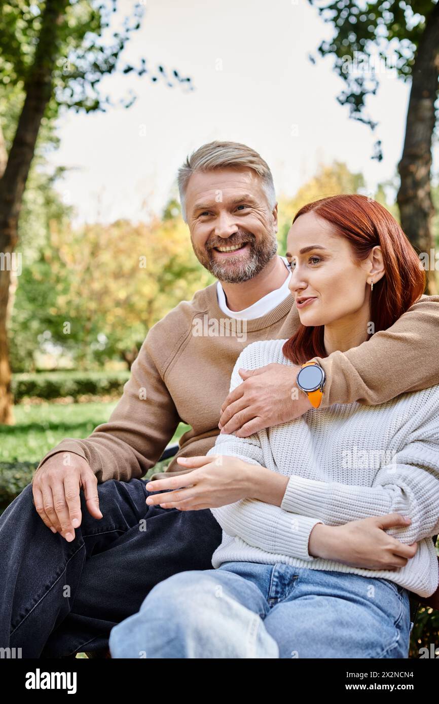 Ein Mann und eine Frau in lässiger Kleidung sitzen auf einer Parkbank und genießen einen friedlichen Moment zusammen. Stockfoto