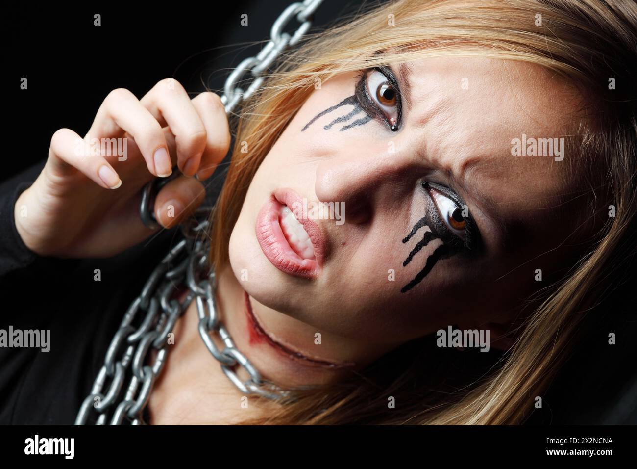 Das böse Zombie-Mädchen mit schwarzen Tränen und durchgeschnittener Kehle hängt an einer Kette auf schwarzem Hintergrund. Stockfoto
