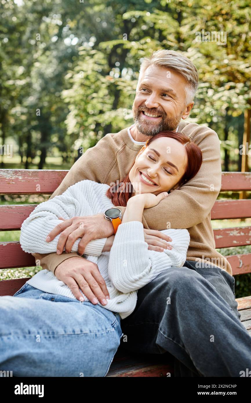 Ein Mann und eine Frau in lässiger Kleidung sitzen auf einer Parkbank und genießen einen friedlichen Moment zusammen. Stockfoto