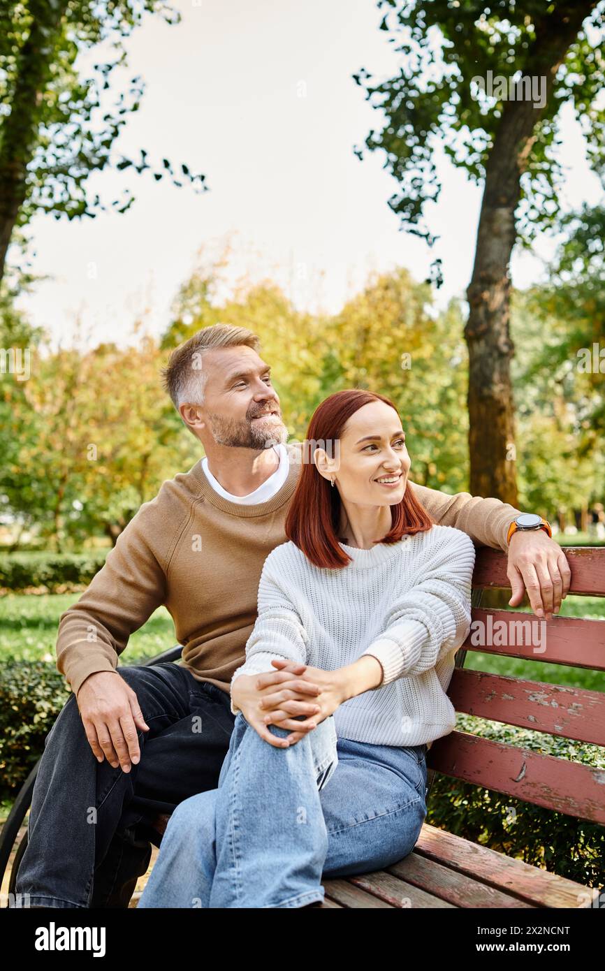 Ein Mann und eine Frau in lässiger Kleidung sitzen auf einer Parkbank und genießen sich Gesellschaft. Stockfoto