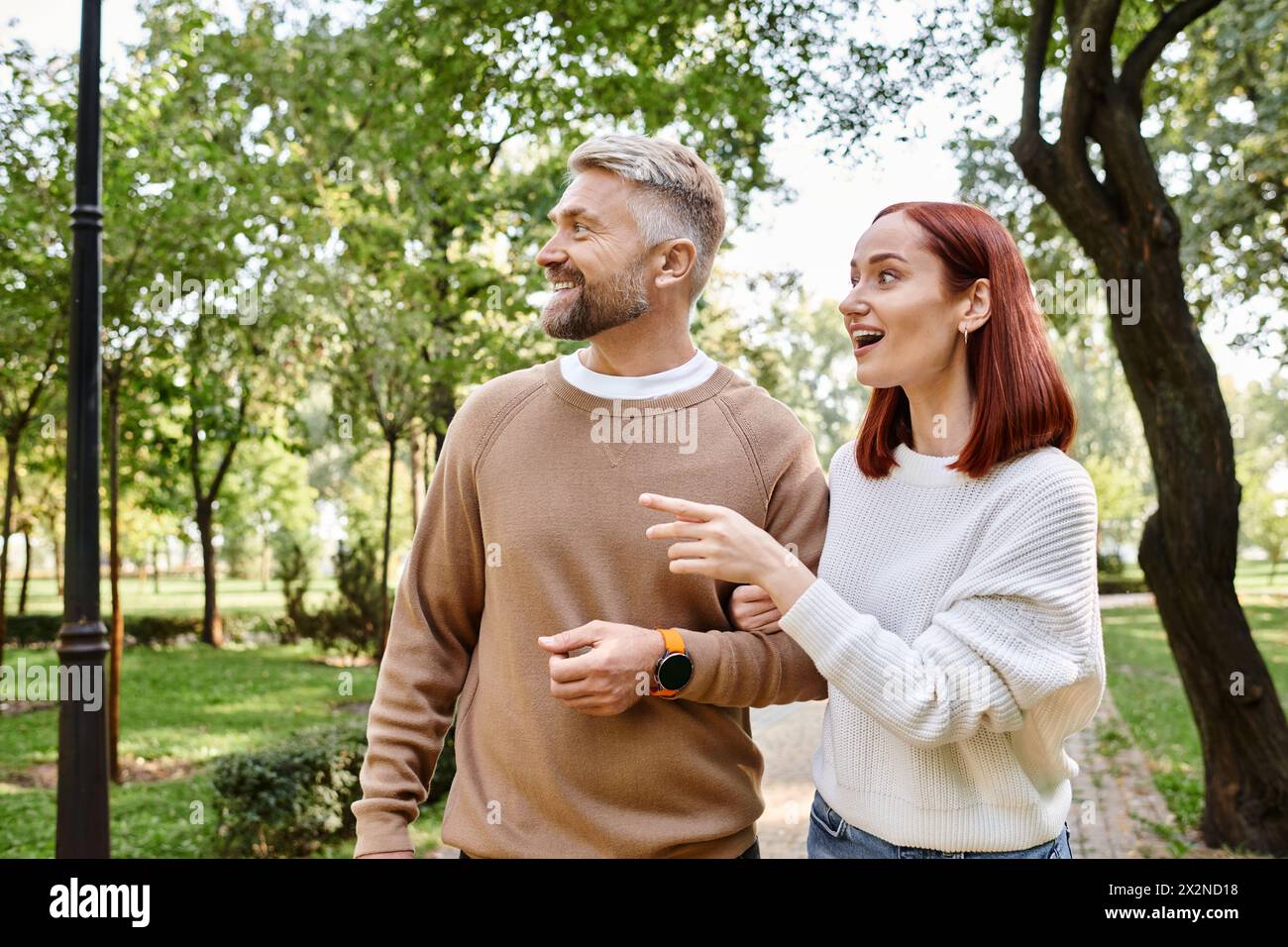 Ein Mann und eine Frau spazieren gemütlich durch einen Park, umgeben von Grün. Stockfoto