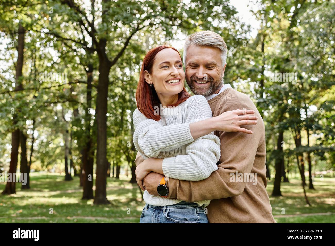Ein erwachsener Mann und eine Frau in lässiger Kleidung umarmen sich liebevoll in einem Park. Stockfoto