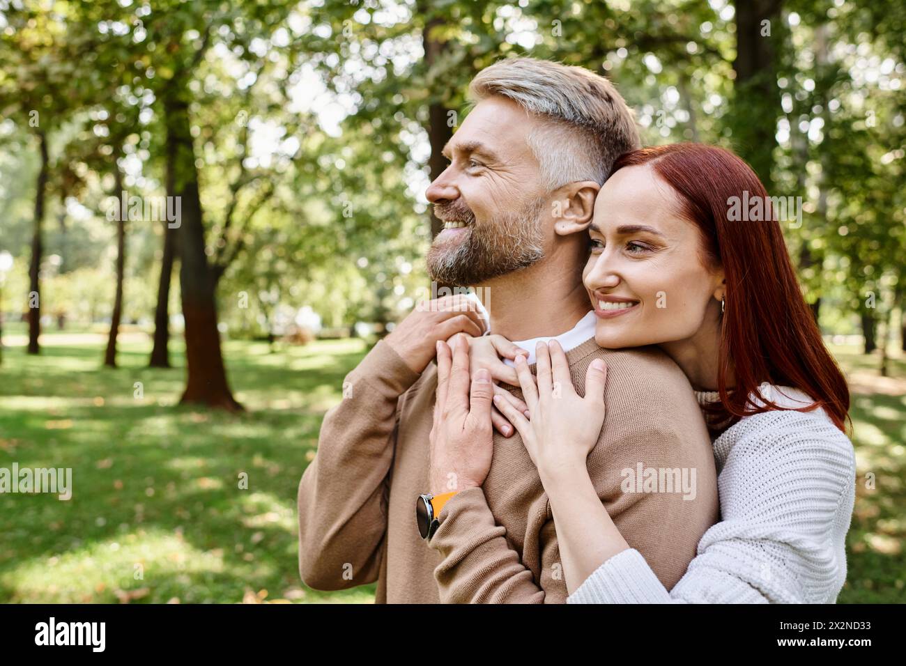 Ein Mann hält eine Frau zärtlich in einem Park, umgeben von Grün und Ruhe. Stockfoto