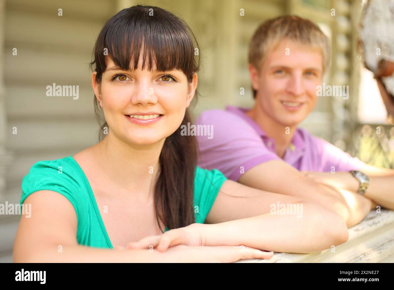 Junges Paar lehnt sich auf die Terrasse eines hölzernen Dorfhauses, konzentriert sich auf die Ehefrau Stockfoto