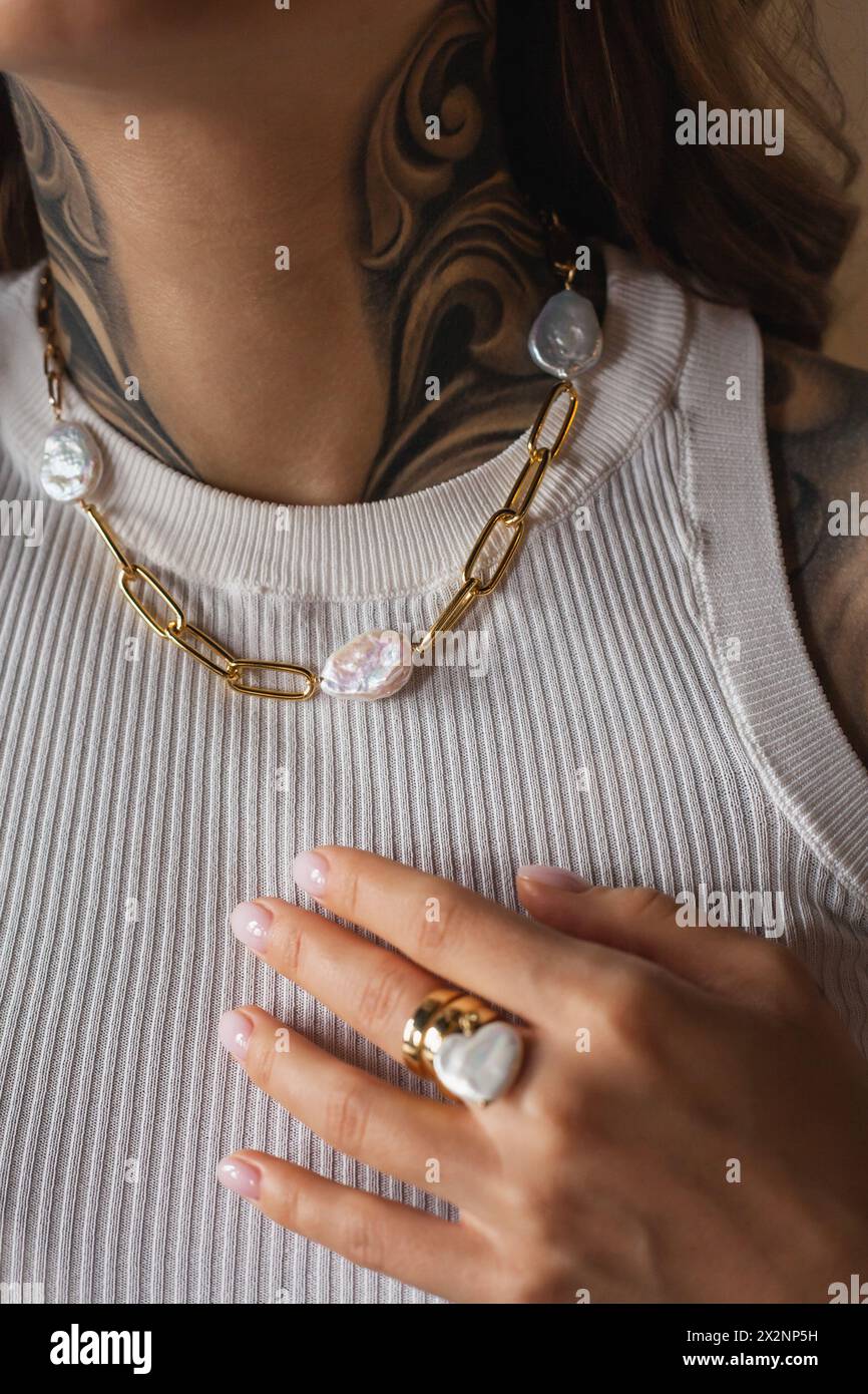 Eine junge Frau mit einem Tattoo zeigt Schmuck an Hals und Arm - eine Halskette mit Süßwasserperlen und einem Ring. Stockfoto