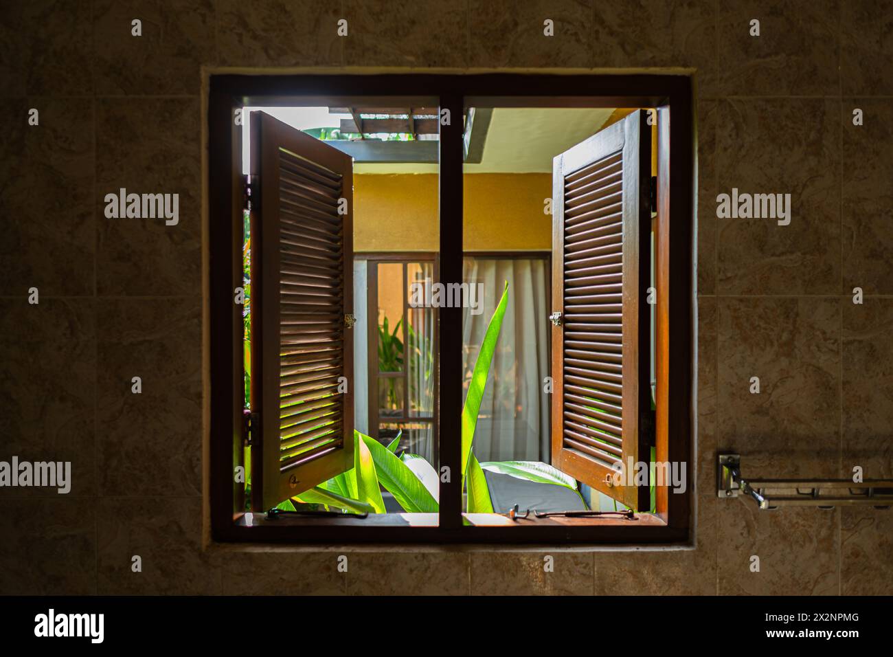 Holzfenster und Fensterläden im Bad öffnen und bieten einen Blick auf tropische Pflanzen und den Garten Stockfoto