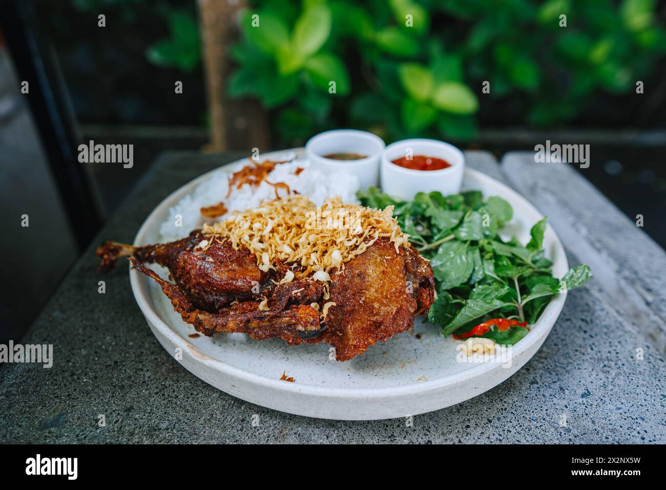 Frittierte Ente mit Reis, grünem Gemüse und zwei Arten von Sambals namens Sambal Matah und Sambal Tomat auf einer weißen Platte Stockfoto