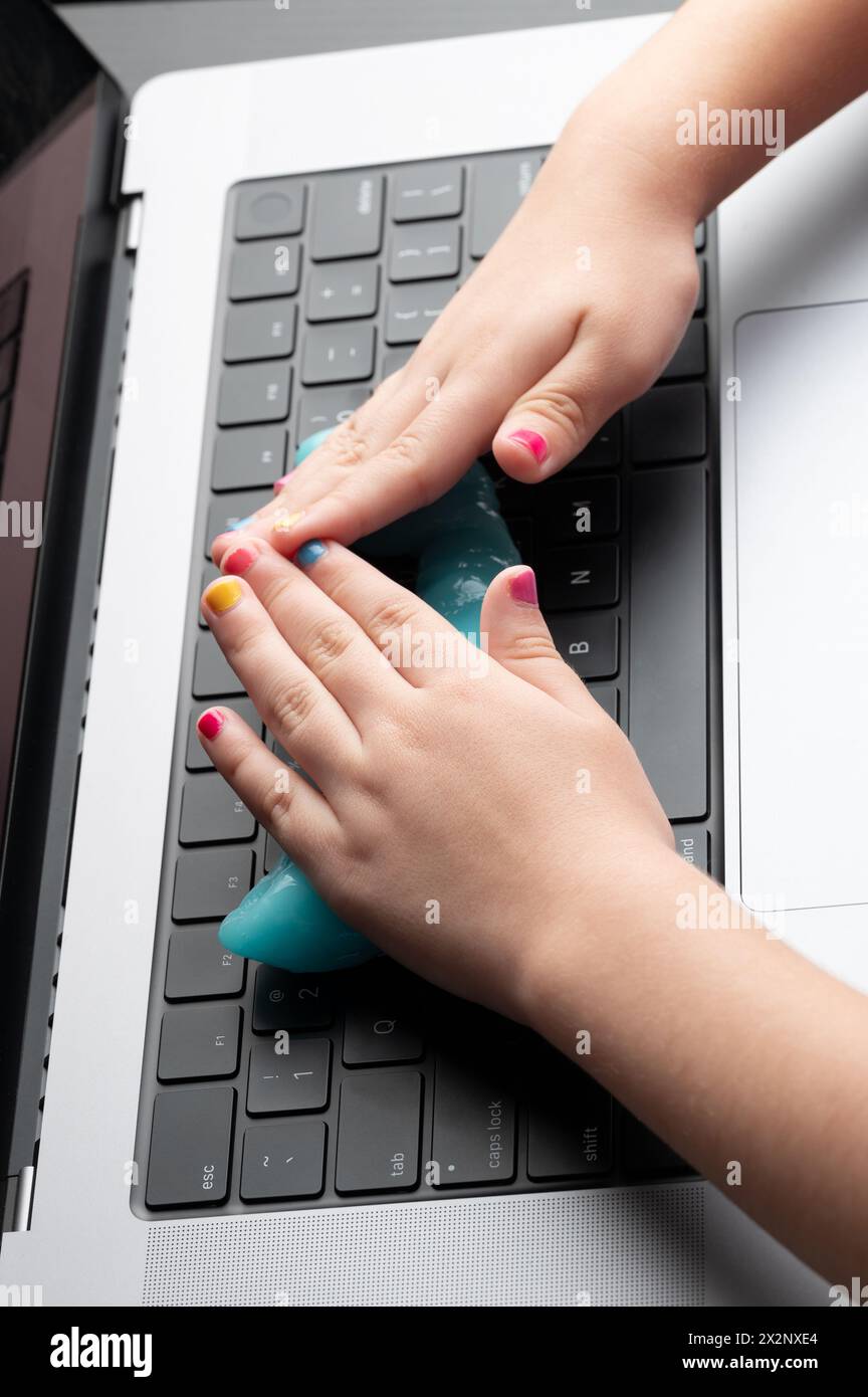 Hände mit bunten Nägeln reinigen die Tastatur eines modernen Laptops Stockfoto