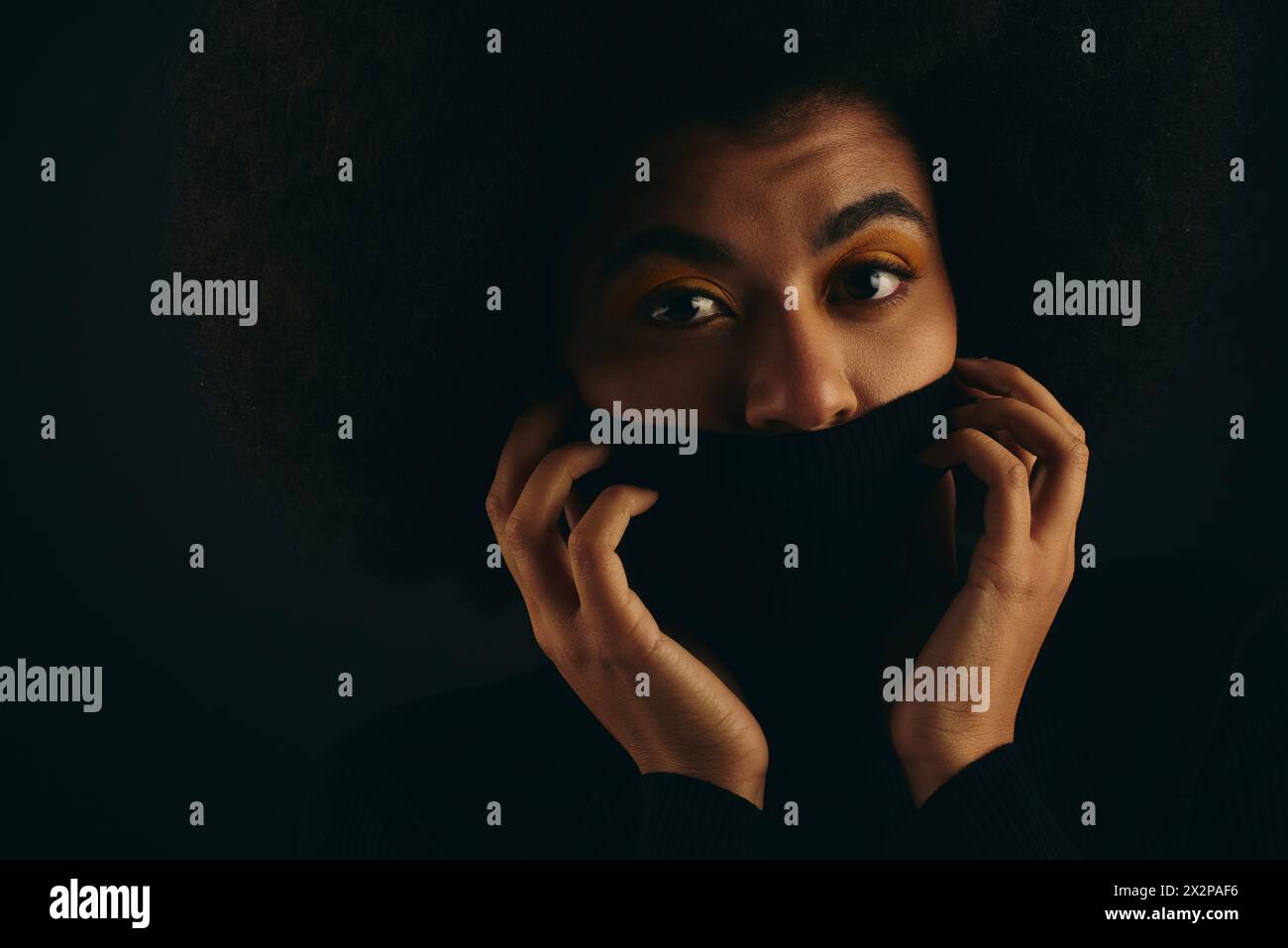 Die afroamerikanische Frau bedeckt das Gesicht stilvoll mit schwarzem Tuch vor einem lebendigen Hintergrund. Stockfoto