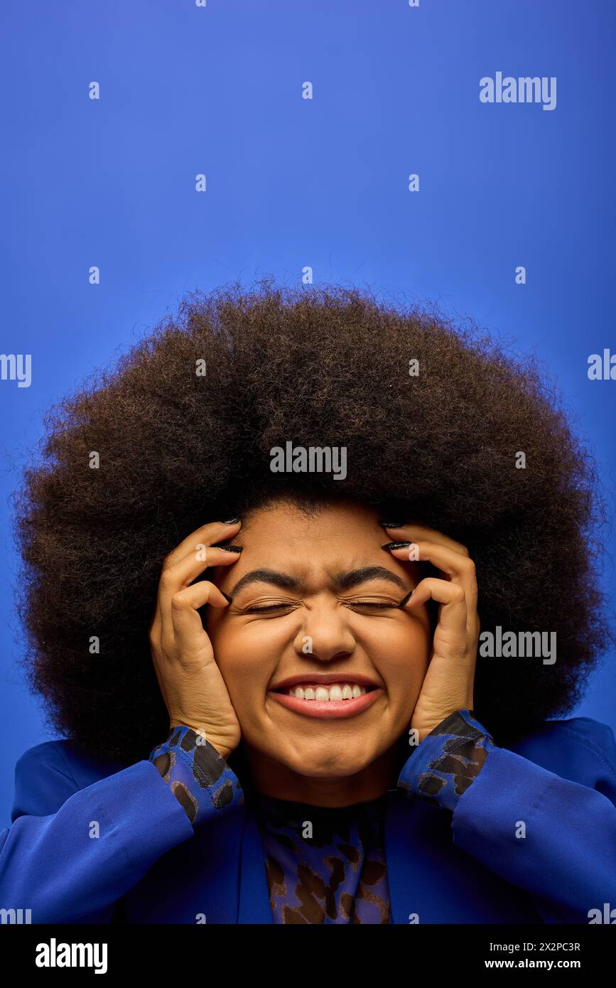 Eine stilvolle afroamerikanische Frau mit lockiger Frisur, die ihre Hände in einem Moment der Reflexion ins Gesicht hält. Stockfoto