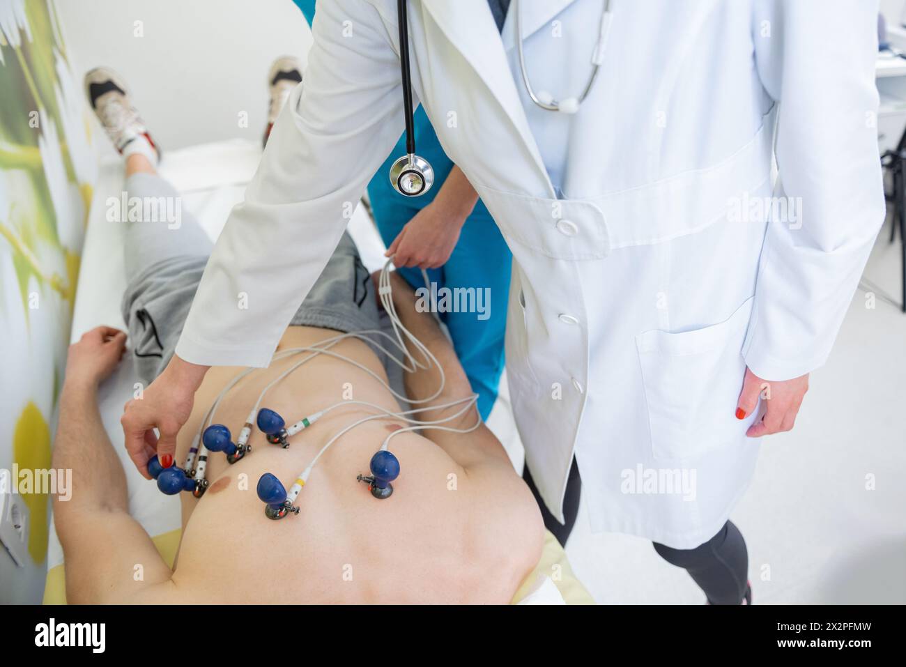 Ein qualifizierter Facharzt bringt EKG-Elektroden zur Herzüberwachung sorgfältig an einen Patienten an Stockfoto