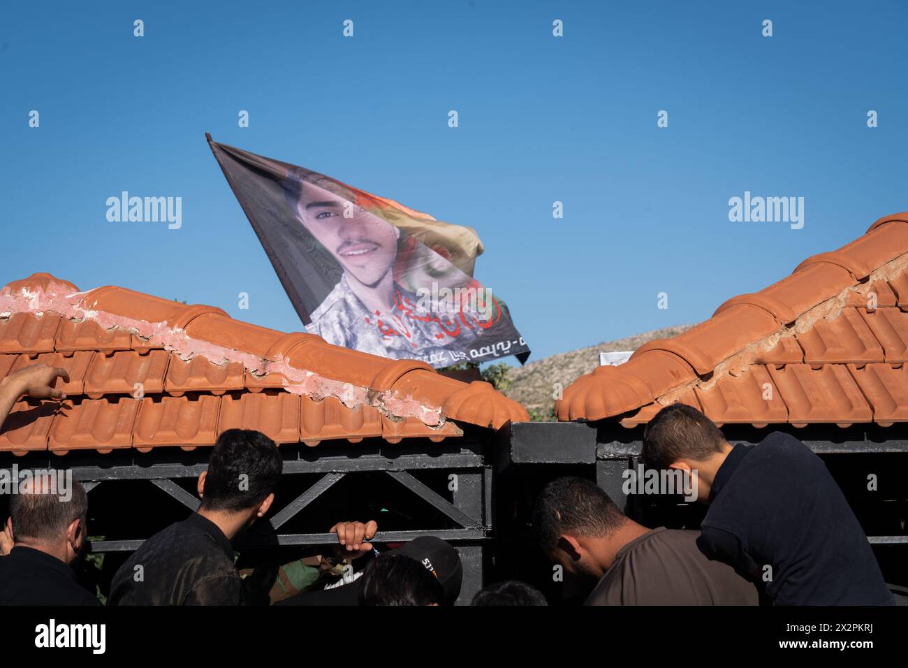 Mansouri, Libanon. April 2024. Eine Flagge mit einem Porträt der Hisbollah, die zuvor getötet wurde, wird während der Beerdigung eines anderen Kämpfers in Mansouri gehisst. Die Hisbollah hielt im Südlibanon eine Beerdigung für ihre Kämpfer ab, die bei einem israelischen Streik getötet wurden. Die israelischen Streitkräfte und die libanesische Gruppe Hisbollah haben ihre grenzüberschreitenden Kämpfe intensiviert und Ängste vor einer Eskalation geweckt, während Israel seinen Krieg gegen Gaza fortsetzt und nachdem Iran und Israel Feuer ausgetauscht haben. (Credit Image: © Ashley Chan/SOPA Images via ZUMA Press Wire) NUR REDAKTIONELLE VERWENDUNG! Nicht für kommerzielle ZWECKE! Stockfoto