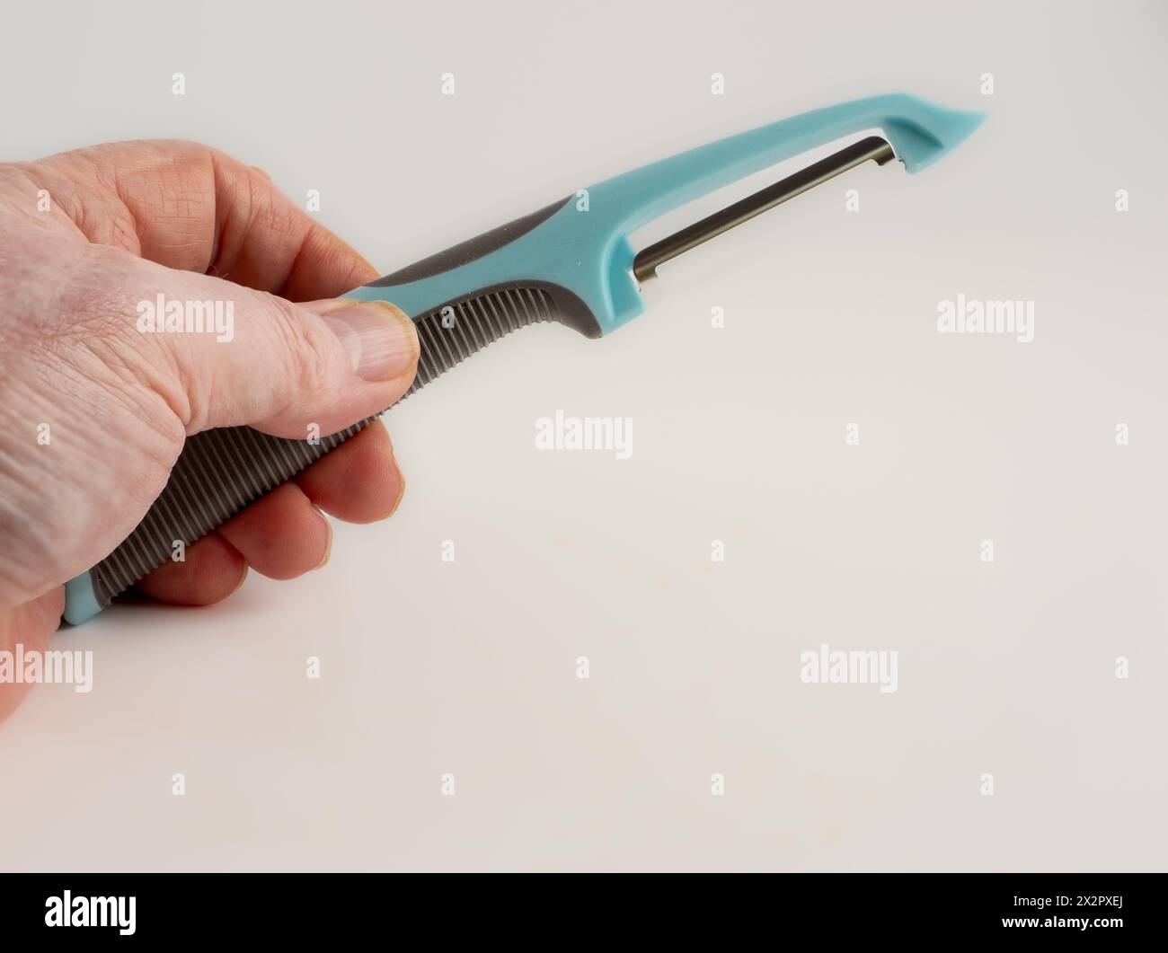 Der Koch hält einen blauen Kartoffelschäler auf weißem Hintergrund Stockfoto
