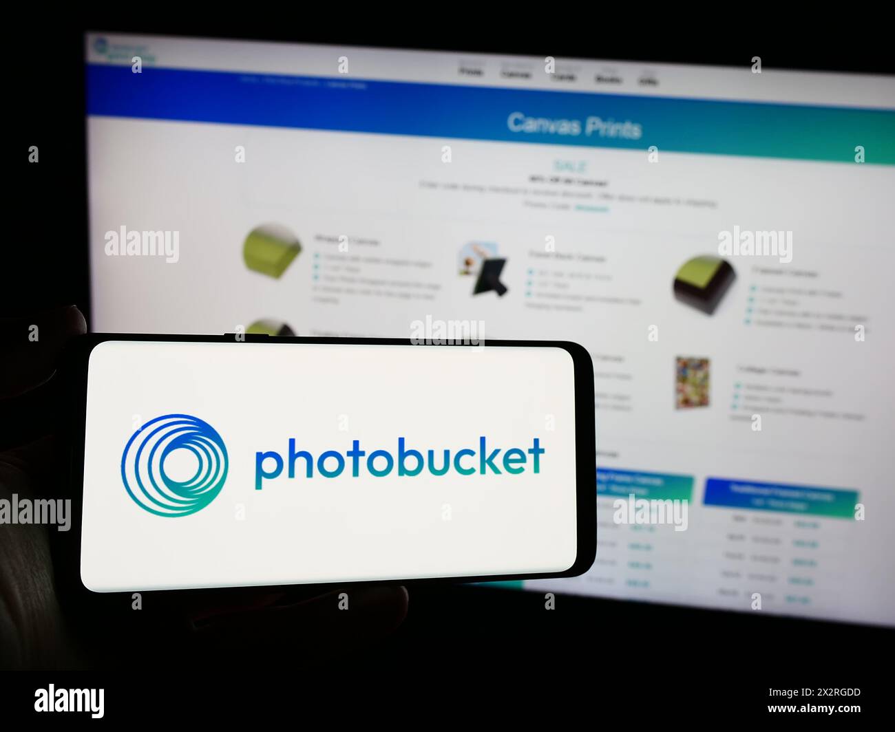 Person, die ein Mobiltelefon mit dem Logo des amerikanischen Bildhosting-Unternehmens Photobucket.com Inc. Vor der Webseite hält. Schwerpunkt auf dem Display des Telefons. Stockfoto