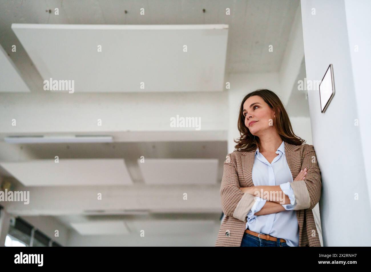 Nachdenkliche Geschäftsfrau, die sich mit moderner Automatisierungstechnik an der Wand im Büro orientiert Stockfoto