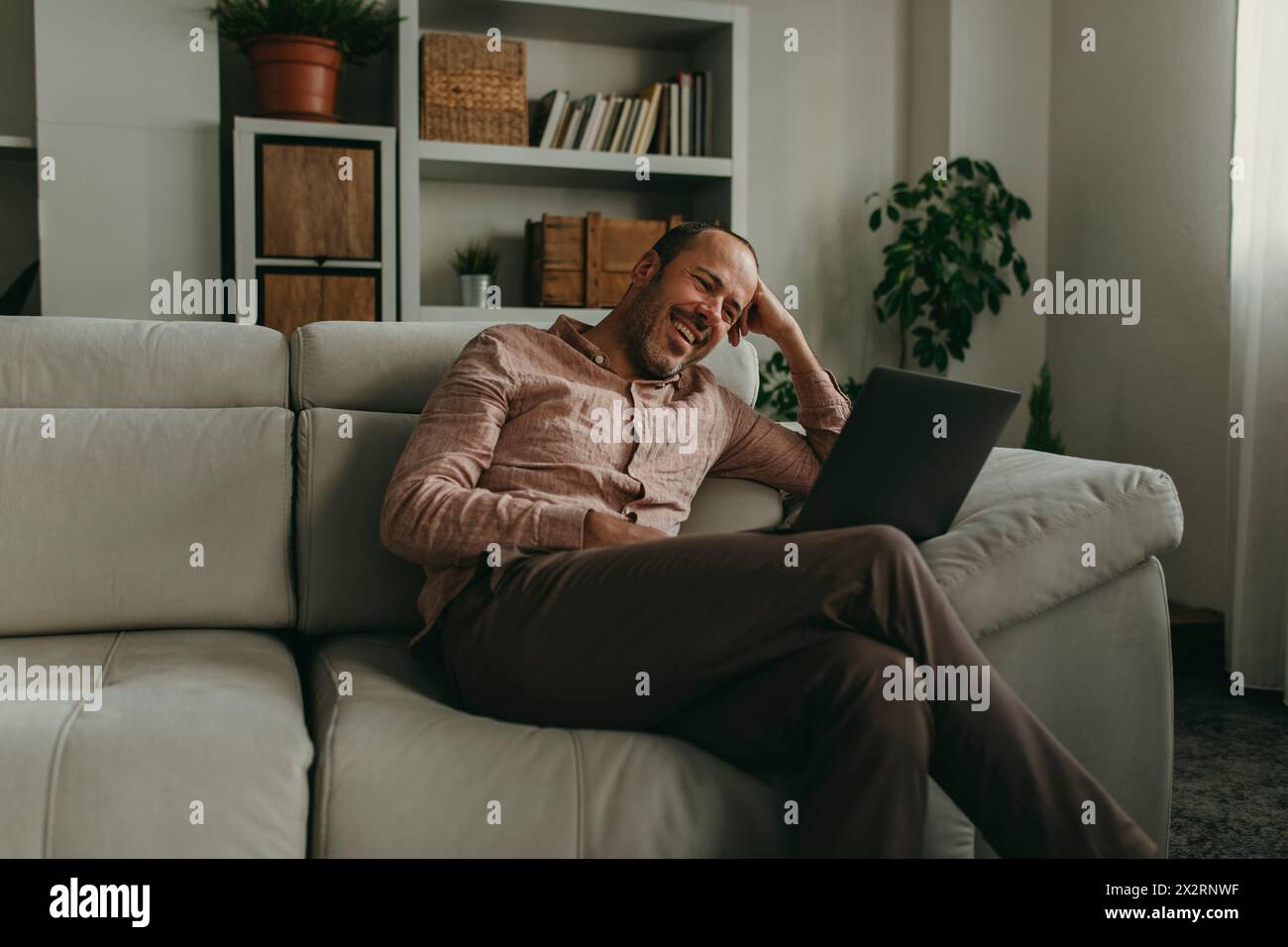 Ein lächelnder Mann, der zu Hause auf einem Laptop Filme ansieht Stockfoto