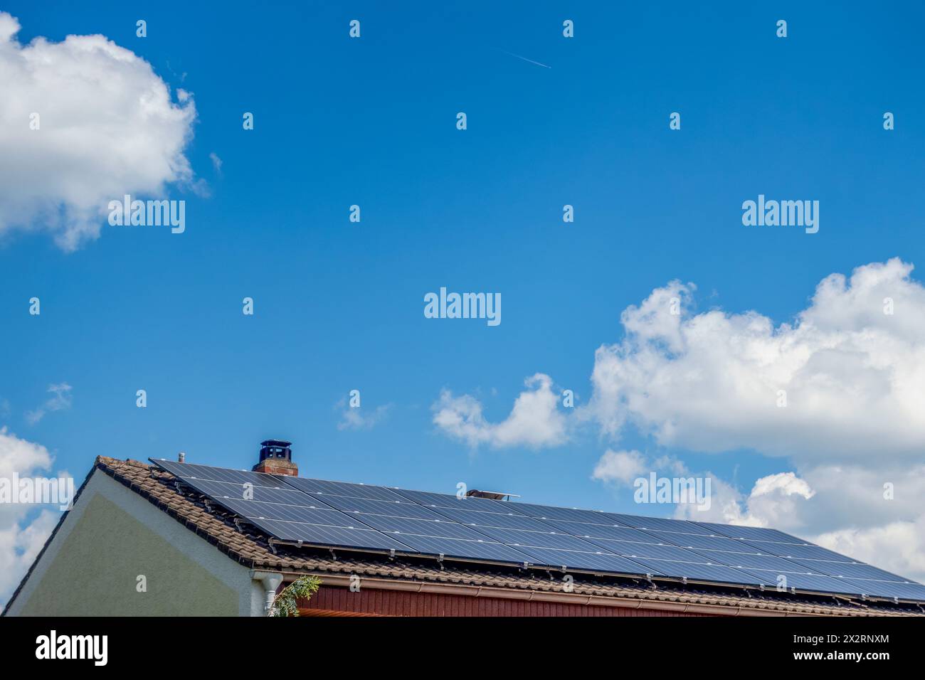 Solarpaneele auf dem Dach des Hauses unter bewölktem blauen Himmel in Bayern, Deutschland Stockfoto