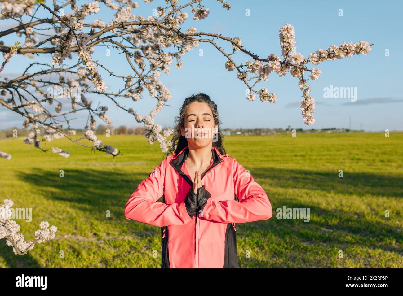 Frau meditiert mit geschlossenen Augen in der Nähe eines Mandelblütenbaums Stockfoto