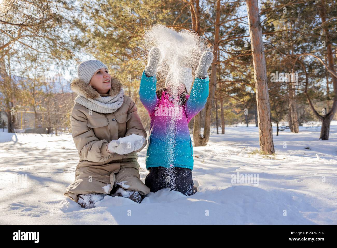 Mädchen, das Schnee in der Nähe der Mutter im Winterwald wirft Stockfoto