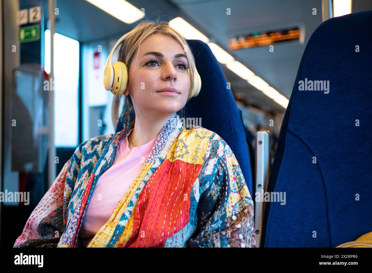 Frau, die Musik über kabellose Kopfhörer hört, sitzt im Zug Stockfoto