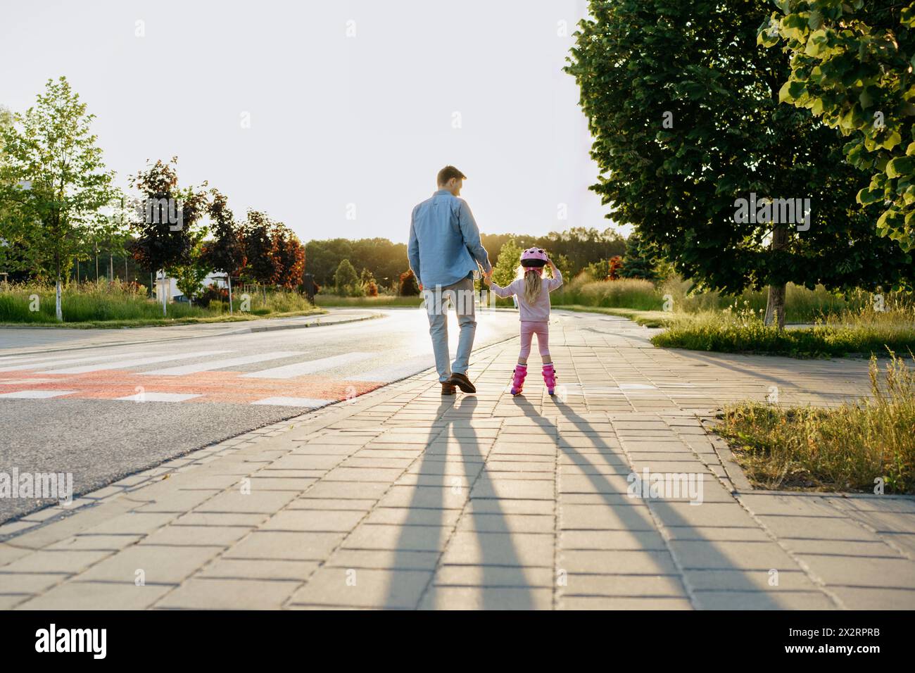 Mann, der die Hand einer Tochter hält, die Rollschuhlaufen auf dem Bürgersteig macht Stockfoto