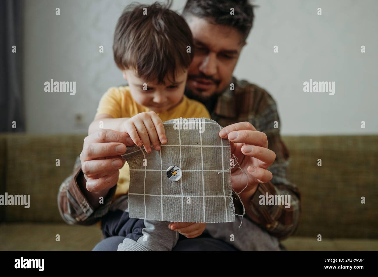 Mann, der Sohn beibringt, zu Hause Knopf auf graues Tuch zu nähen Stockfoto